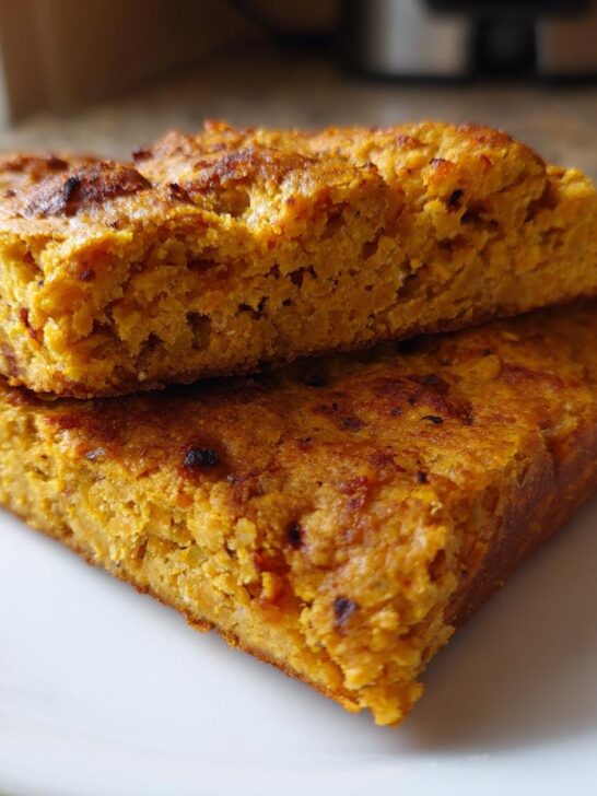 Two thick, golden-orange squares of High Protein Red Lentil Flatbread stacked on a white plate.