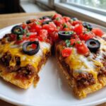 A close-up of Homemade Mexican Pizza, cut in half, topped with melted cheese, seasoned beef, diced tomatoes, and black olives.