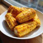 Close-up of several glistening ears of Honey Butter Skillet Corn piled on a white plate.