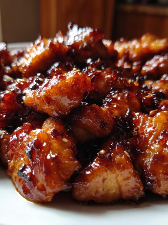 Close-up of bite-sized pieces of Honey Garlic Chicken coated in a thick, glossy, dark brown glaze and sprinkled with sesame seeds.