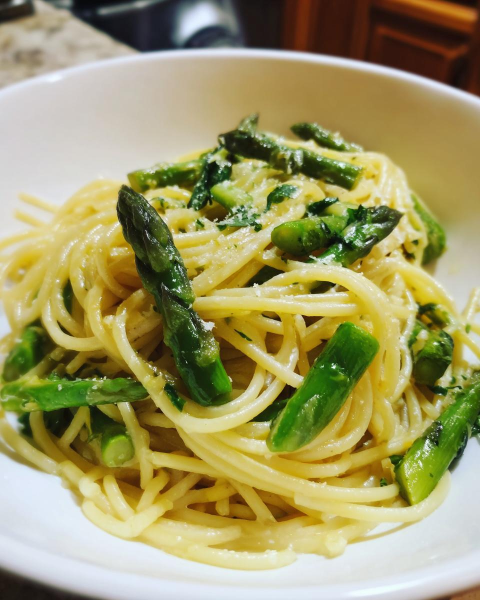 A close-up view of a serving of Lemon Asparagus Pasta tossed in a light sauce and topped with bright green asparagus spears and grated cheese.