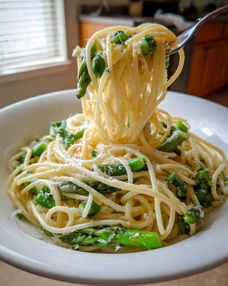 A fork lifting a twirl of spaghetti from a bowl of Lemon Asparagus Pasta topped with Parmesan.