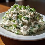 A mound of creamy Lemon Basil Chicken Salad featuring shredded chicken, celery, and green herbs, served on a white plate.