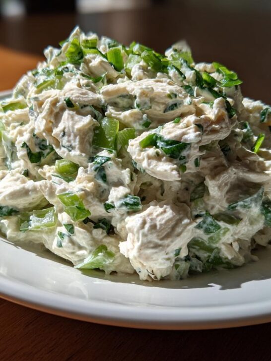 A mound of creamy Lemon Basil Chicken Salad featuring shredded chicken, celery, and green herbs, served on a white plate.