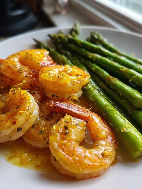 Close-up of Lemon Garlic Shrimp And Asparagus coated in a bright yellow sauce on a white plate.