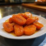 Close-up of shiny, orange Maple Glazed Carrots piled on a small white serving dish.