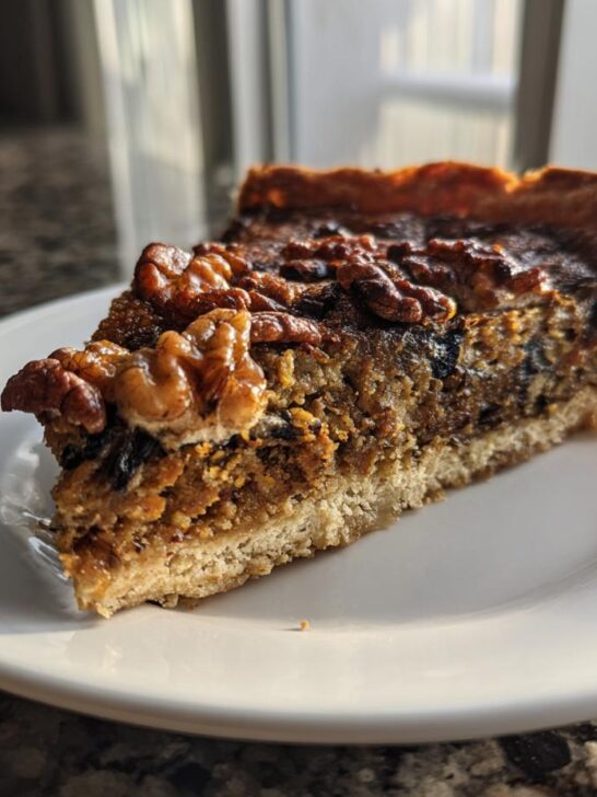 A close-up slice of Mushroom Lentil And Walnut Tart topped with whole walnuts, sitting on a white plate.