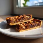 Two rectangular slices of Mushroom Lentil And Walnut Tart stacked on a white plate, topped with walnuts.