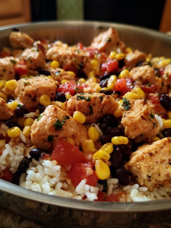 Close-up of a One Pan Chicken Burrito Bowl with seasoned chicken, rice, corn, black beans, and tomatoes in a metal skillet.