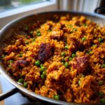 Close-up of savory One Pan Spanish Chicken and Rice mixed with bright green peas, cooked in a stainless steel skillet.