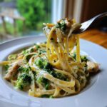 A fork lifting creamy fettuccine noodles, chicken, and broccoli from a bowl of One Pot Chicken Broccoli Alfredo.
