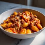 Close-up of a bowl filled with One Pot Creamy Beef And Shells, topped with melted cheese.