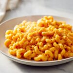 A close-up of steaming, creamy One Pot Pumpkin Mac And Cheese topped with black pepper.
