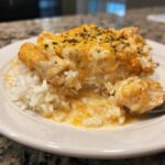 A close-up of a serving of One Pot Queso Chicken And Rice over white rice, topped with melted cheese and parsley.