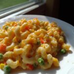 A close-up, appetizing shot of creamy One Pot Veggie Mac And Cheese featuring elbow macaroni, peas, and carrots.
