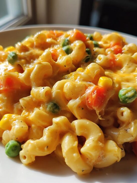 Close-up of creamy One Pot Veggie Mac And Cheese with peas, carrots, and corn on a white plate.