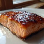 A close-up, beautifully caramelized fillet of Orange Glazed Salmon resting on a white plate.