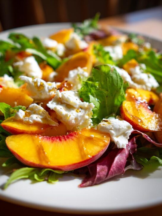 Close-up of a vibrant Peach Burrata Salad featuring fresh peaches, creamy cheese, and arugula greens.