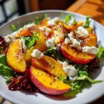 Close-up of a vibrant Peach Burrata Salad featuring bright yellow peach slices, creamy white burrata, and mixed greens.