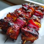 Close-up of juicy Peruvian Grilled Chicken Skewers with charred edges, red onion, and yellow bell pepper on a white plate.