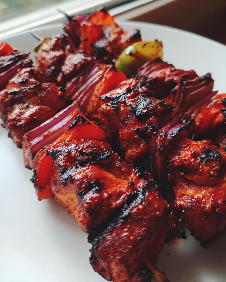 Close-up of vibrant, charred Peruvian Grilled Chicken Skewers with red onion and peppers on a white plate.