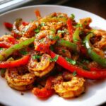 Close-up of seasoned Sheet Pan Shrimp Fajitas mixed with vibrant red and green bell pepper strips, garnished with parsley.