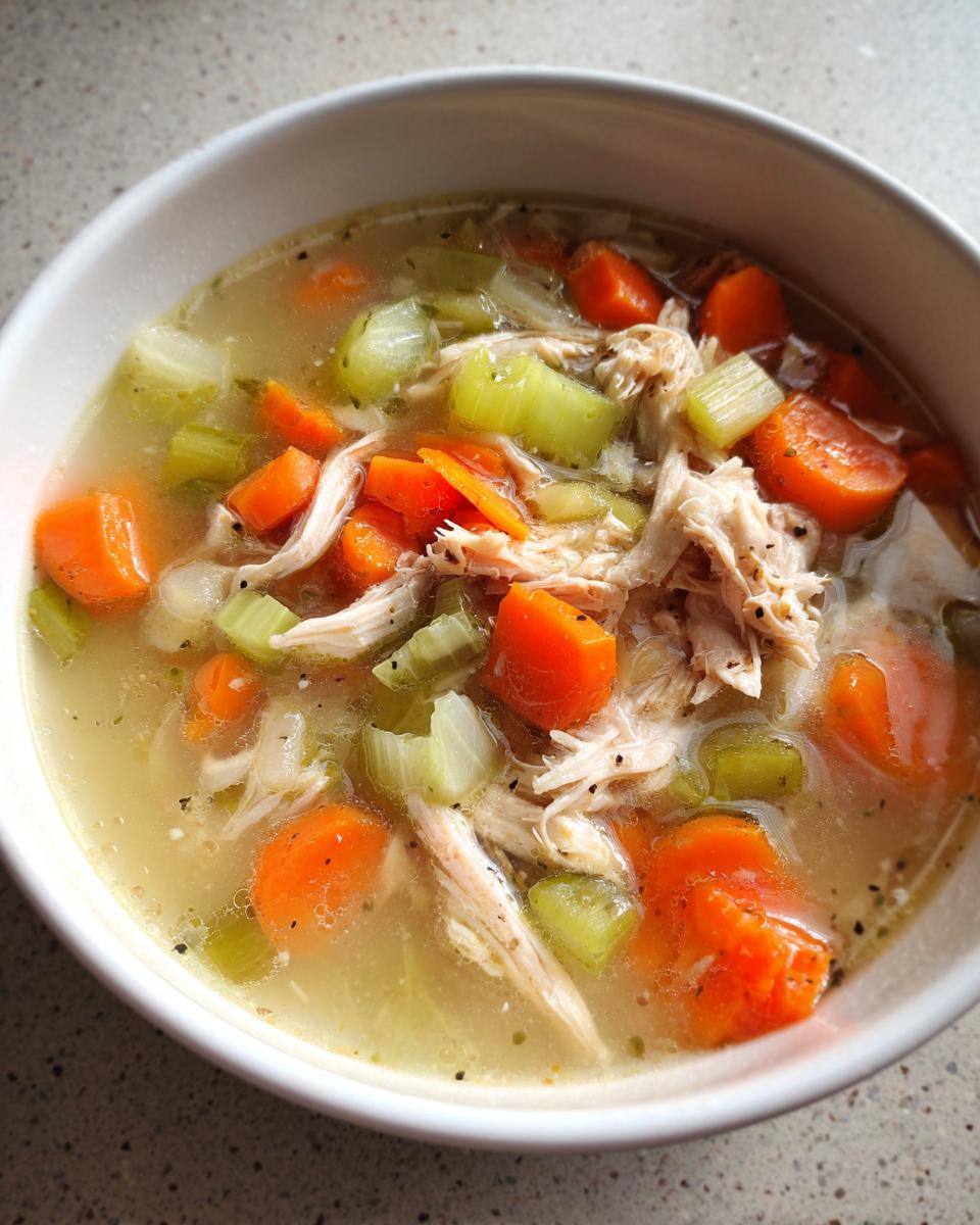 Close-up of a bowl of shredded chicken soup with large chunks of carrots and celery, perfect for high protein low carb soups.