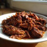 A close-up of richly seasoned, shredded Slow Cooker Beef Barbacoa piled high on a white plate.