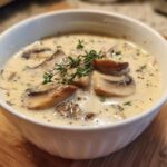 Close-up of a white bowl filled with Skinny Cream Of Mushroom Soup, topped with sliced mushrooms and fresh thyme.