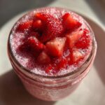 Close-up, top-down view of bright pink Strawberry Chia Seed Pudding topped with diced fresh strawberries and foam.