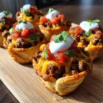 Close-up of several golden Taco Pizza Appetizer Bites filled with seasoned beef, melted cheese, tomatoes, and sour cream.