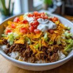 A close-up of a fully loaded Taco Rice Bowl With Doritos, featuring seasoned ground beef, rice, lettuce, cheese, sour cream, and salsa.