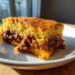 Close-up of a moist slice of Texas Tamale Pie showing the golden cornbread top and savory, seasoned meat filling layer.