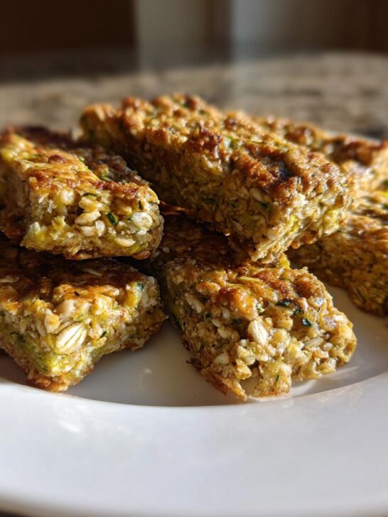 A stack of golden-brown Vegan Zucchini And Oatmeal Sticks resting on a white plate.