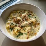 A close-up view of a bowl of White Lasagna Soup featuring pasta pockets in a creamy sauce, topped with grated cheese and herbs.