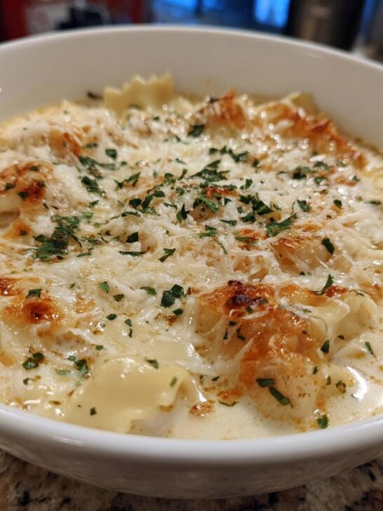 A close-up photo of a serving of White Lasagna Soup in a white bowl, topped with melted cheese and parsley.